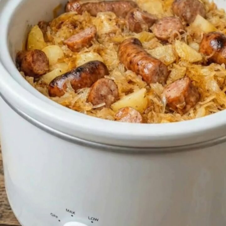 A steaming portion of sliced smoked kielbasa, tender potatoes, and sauerkraut on a white plate.