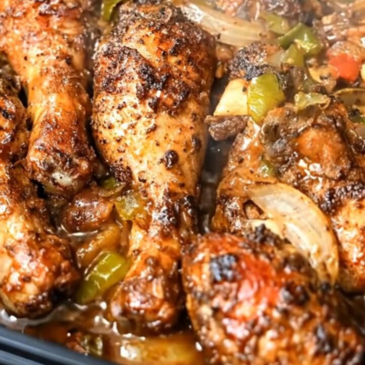A close-up of sticky garlic herb chicken drumsticks with caramelized bell peppers and onions in a roasting dish.