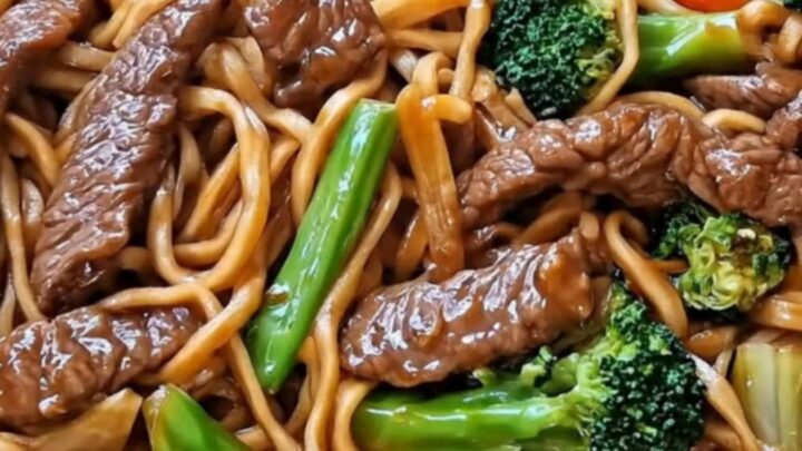 A steaming portion of beef and broccoli lo mein being lifted from a black skillet with kitchen tongs.