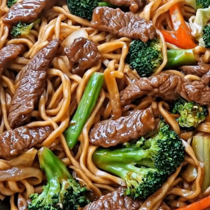 A steaming portion of beef and broccoli lo mein being lifted from a black skillet with kitchen tongs.