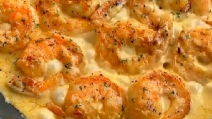 A close-up shot of golden seared shrimp in a creamy garlic sauce inside a black skillet with steam rising.