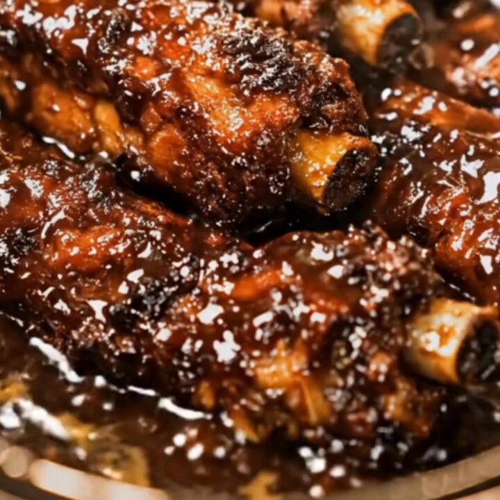 A close-up view of tender, glazed BBQ ribs being lifted from a slow cooker with tongs.