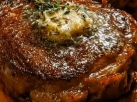 A perfectly seared ribeye steak resting on a wooden board with melting garlic herb butter.