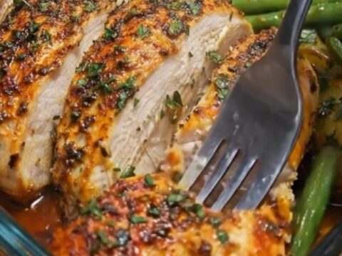 A glass baking dish filled with herb-roasted chicken thighs, baby potatoes, and green beans.