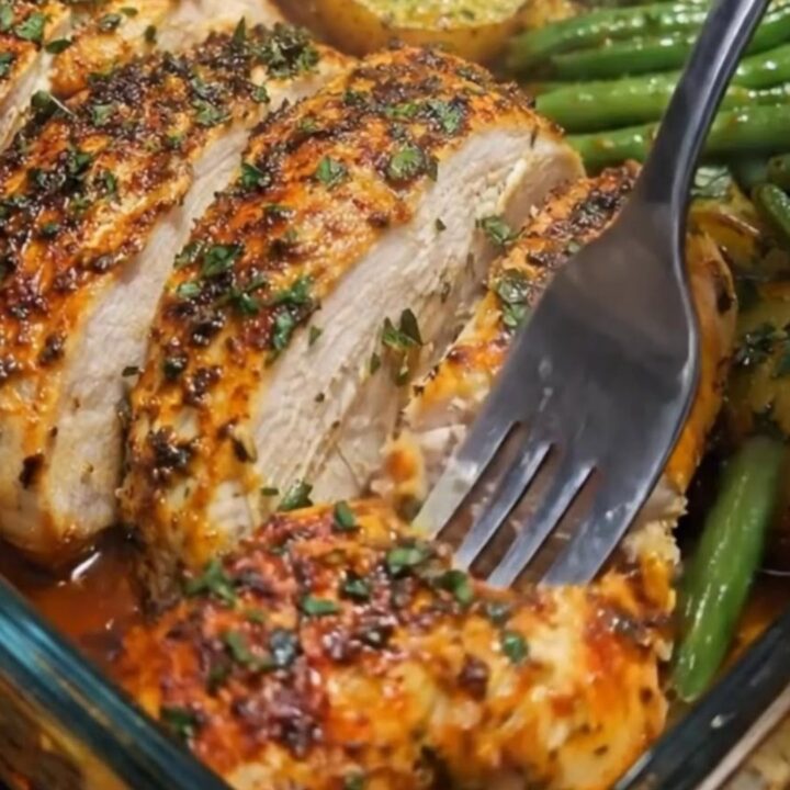 A glass baking dish filled with herb-roasted chicken thighs, baby potatoes, and green beans.