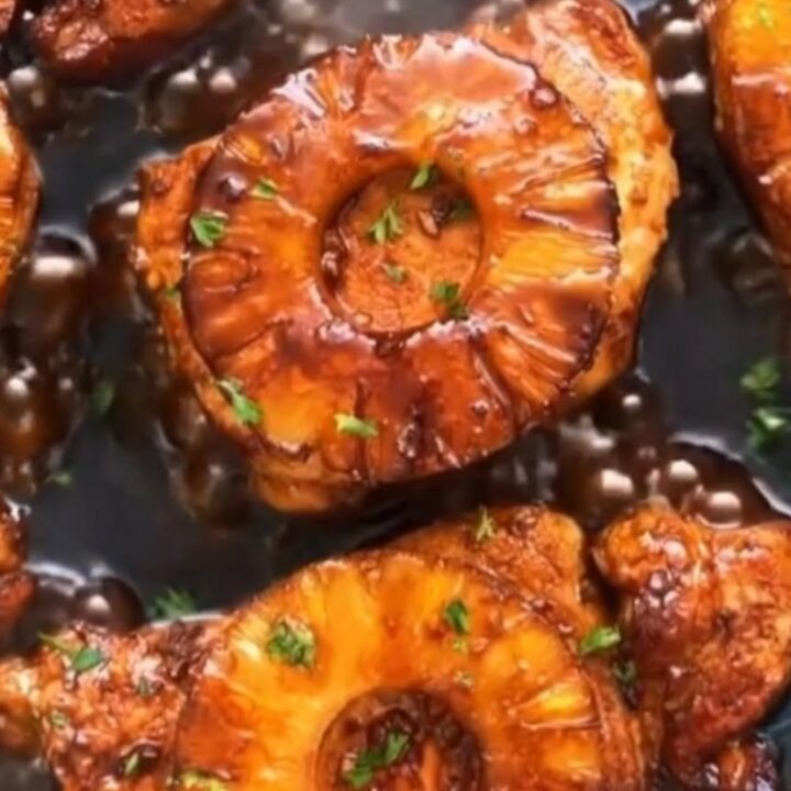 A glossy, teriyaki-glazed pork chop with a caramelized pineapple slice in a sizzling skillet.