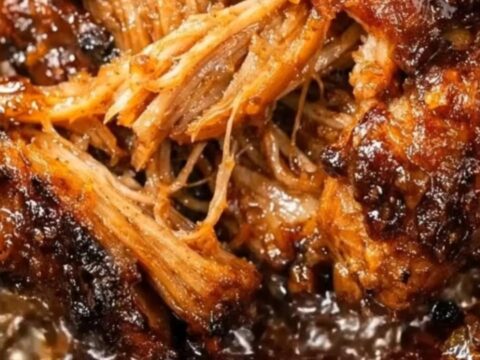 A close-up of tender, glossy pulled pork in a slow cooker with steam rising.