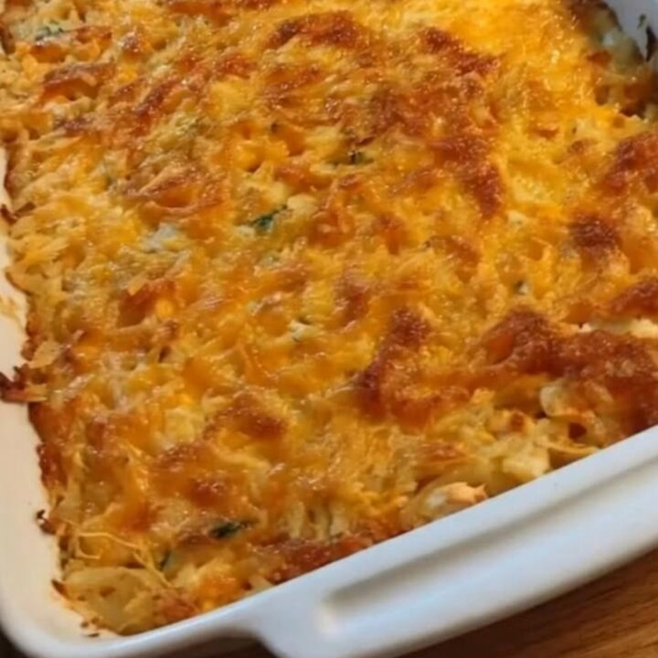 A serving of chicken hash brown casserole being scooped with a spoon, showing steam and melted cheese.