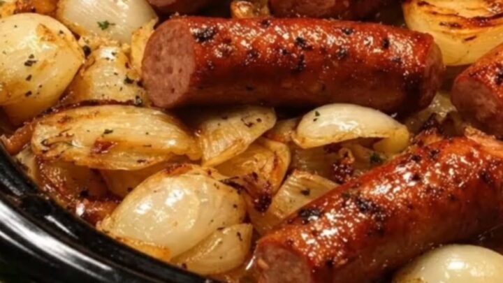 A close-up of juicy, browned sausage links and golden caramelized onions in a black slow cooker.