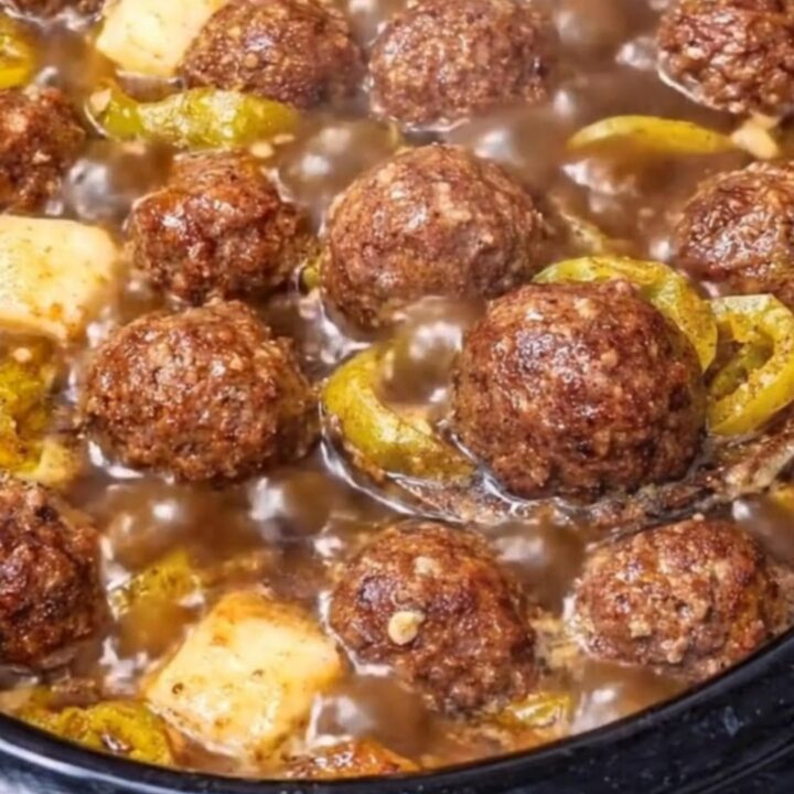 A close-up of tender, glazed meatballs in a slow cooker, covered in a rich, tangy sauce with sliced pepperoncini peppers.