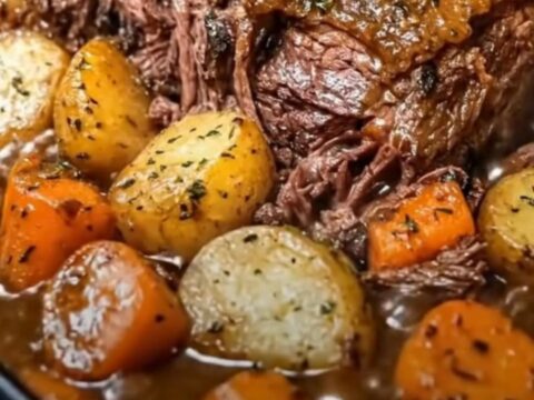 A classic pot roast in a roasting pan with tender beef, golden potatoes, and glazed carrots.