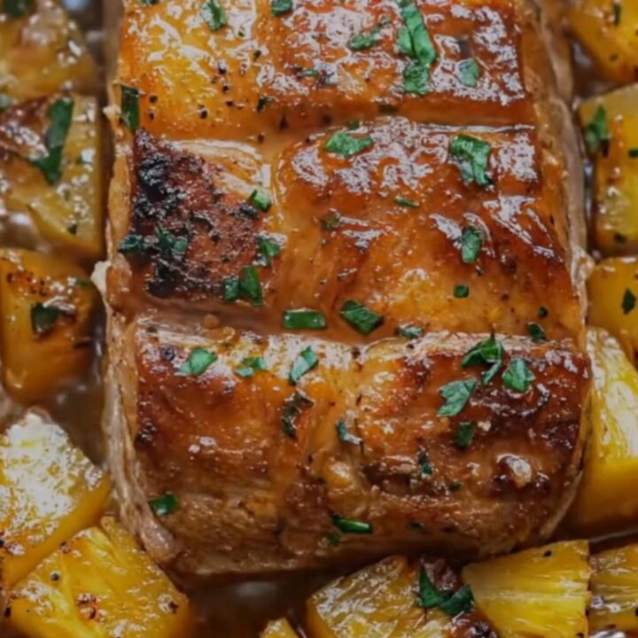 A juicy, slow-cooked pork loin topped with pineapple chunks and fresh parsley.