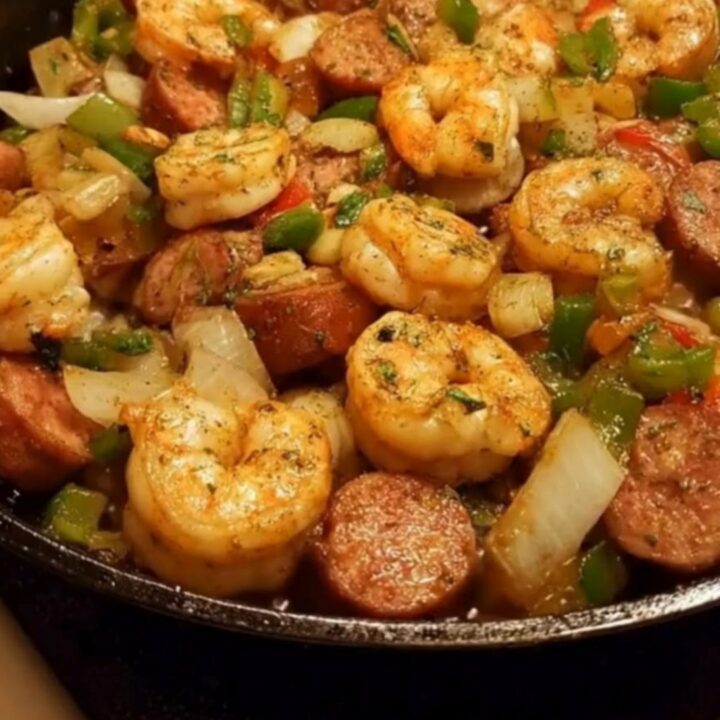 A cast-iron skillet filled with sizzling Cajun shrimp, sliced andouille sausage, and vibrant sautéed bell peppers.