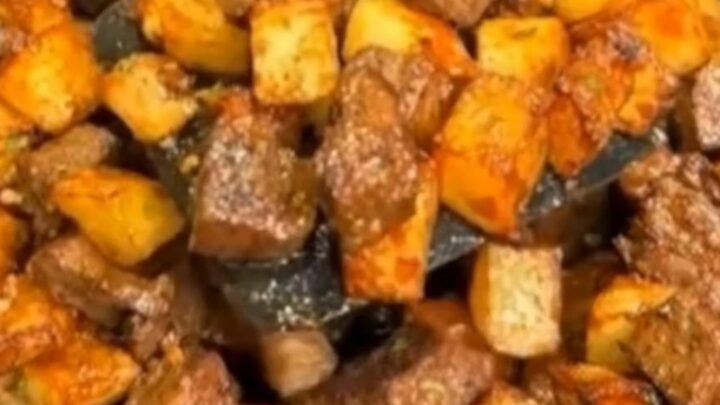 A cast-iron skillet filled with sizzling, golden-brown steak bites and crispy cubed potatoes in garlic butter.