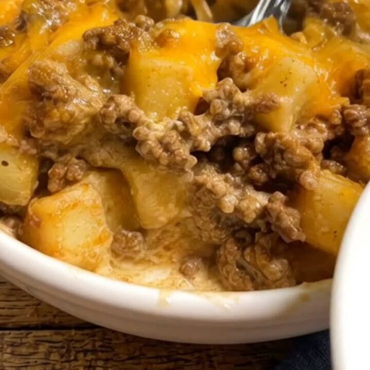 A white bowl filled with creamy taco seasoned ground beef, tender potatoes, and gooey melted cheddar cheese.