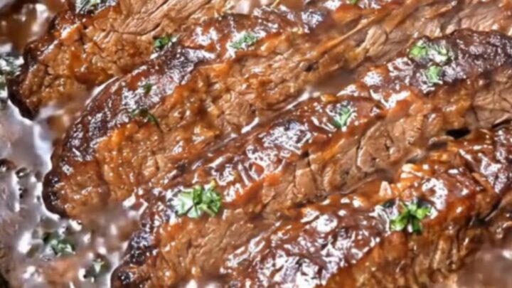 A close-up of tender, slow-cooked brisket slices glistening with rich, dark barbecue sauce on a white plate.