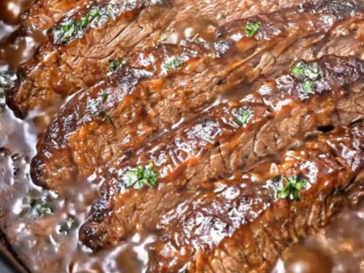 A close-up of tender, slow-cooked brisket slices glistening with rich, dark barbecue sauce on a white plate.