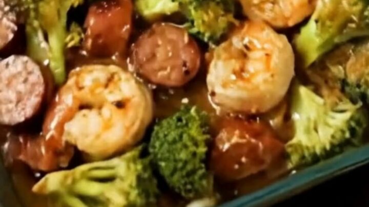 A glass baking dish filled with roasted shrimp, sliced sausage, and bright green broccoli florets.