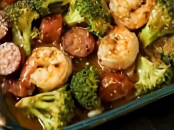 A glass baking dish filled with roasted shrimp, sliced sausage, and bright green broccoli florets.