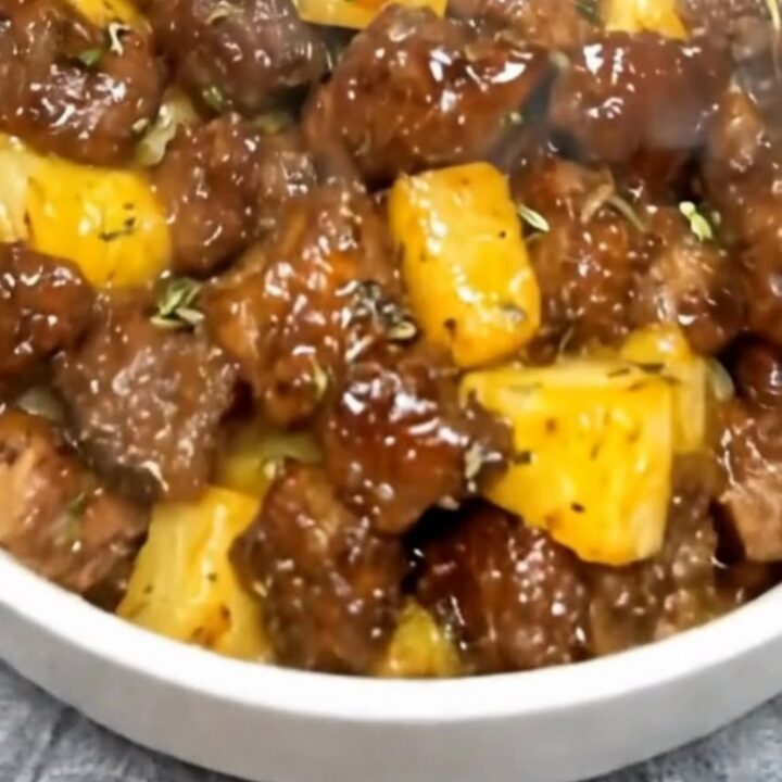 A close-up of glazed sticky pineapple steak bites served in a white bowl with steam rising.