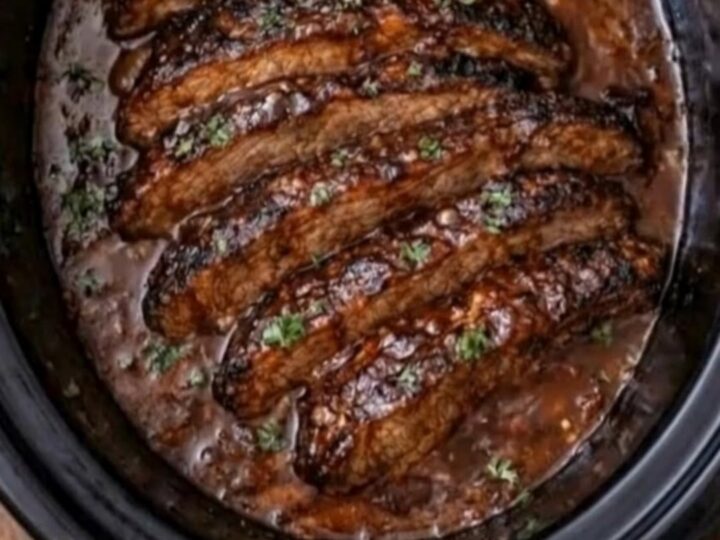 A close-up of tender, sliced BBQ brisket with a glossy glaze resting in a slow cooker.