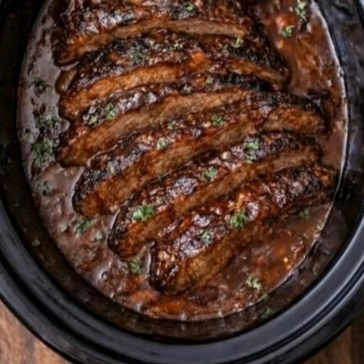 A close-up of tender, sliced BBQ brisket with a glossy glaze resting in a slow cooker.