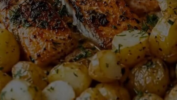 Herb-crusted salmon fillet with roasted baby potatoes in a glass dish.