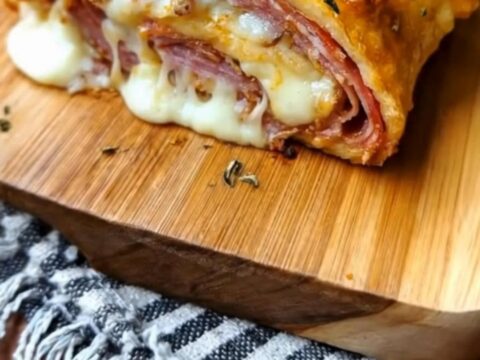A golden, herb-crusted stromboli sitting on a wooden board with a dramatic cheese pull from a freshly cut slice.