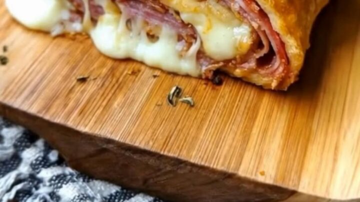 A golden, herb-crusted stromboli sitting on a wooden board with a dramatic cheese pull from a freshly cut slice.