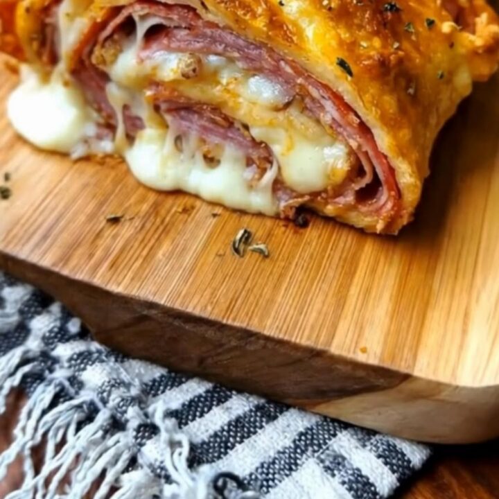 A golden, herb-crusted stromboli sitting on a wooden board with a dramatic cheese pull from a freshly cut slice.