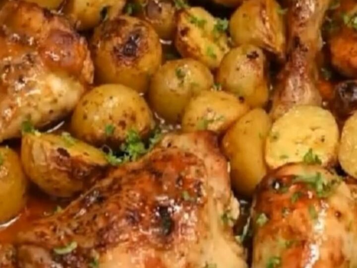 A stainless steel roasting pan filled with golden-brown honey garlic chicken thighs and roasted baby potatoes.