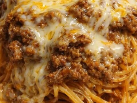 A steaming, cheesy beef spaghetti dish served in a white baking dish with a fork pulling up a portion.