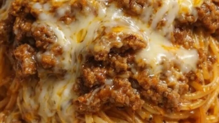A steaming, cheesy beef spaghetti dish served in a white baking dish with a fork pulling up a portion.