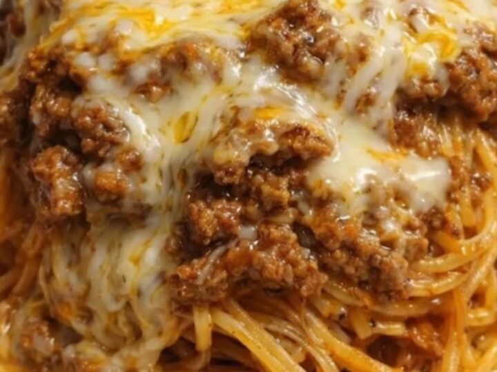 A steaming, cheesy beef spaghetti dish served in a white baking dish with a fork pulling up a portion.