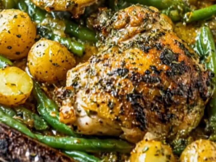 Crispy golden-brown chicken thighs served alongside roasted baby potatoes and fresh green beans on a dark sheet pan.