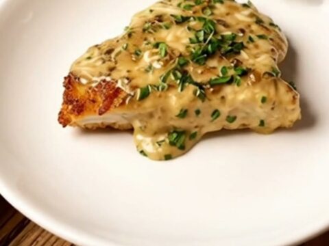 A crispy, golden-brown parmesan-crusted chicken breast cutlet served on a white plate with rich creamy herb sauce.