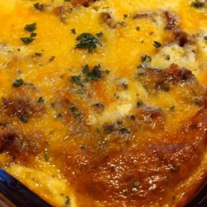 A close-up shot of a spatula lifting a steaming, ultra-cheesy slice of egg casserole from a glass dish.