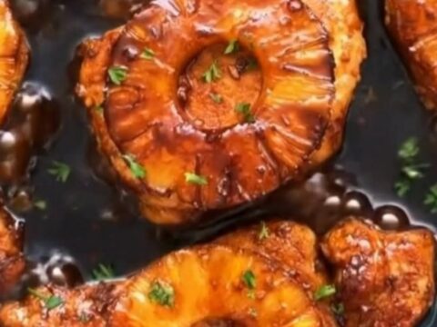 Sticky pineapple teriyaki pork chops glazed in a dark sauce with caramelized pineapple rings in a skillet.