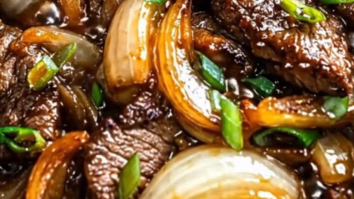 A close-up of glossy beef slices and caramelized onions in a cast-iron skillet, with steam rising.