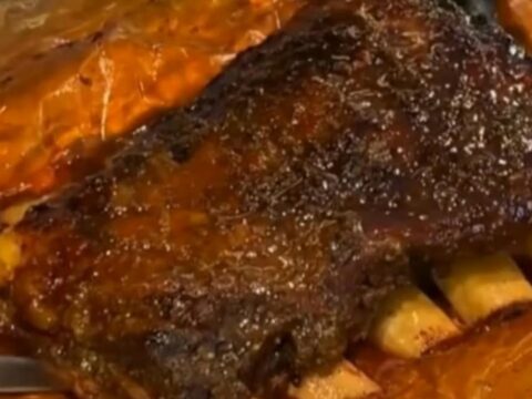 A rack of dark, glazed smoked beef ribs resting on butcher paper in a cozy kitchen setting.