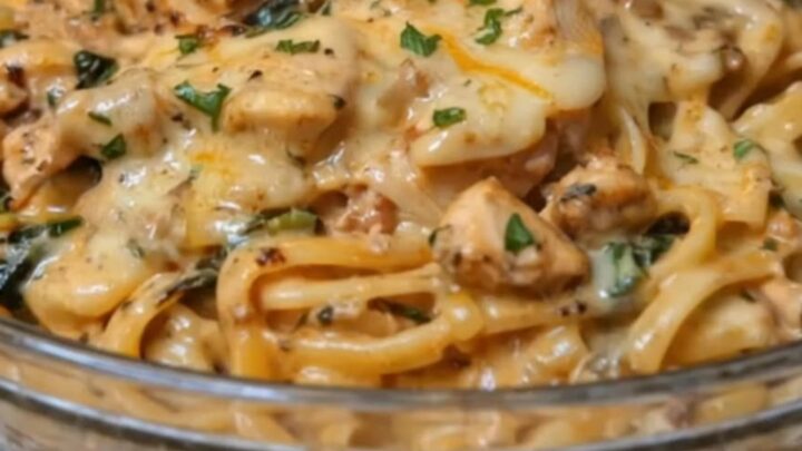 A close-up view of creamy chicken linguine with fresh spinach and melted cheese on a white plate.