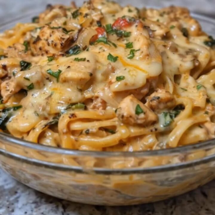 A close-up view of creamy chicken linguine with fresh spinach and melted cheese on a white plate.