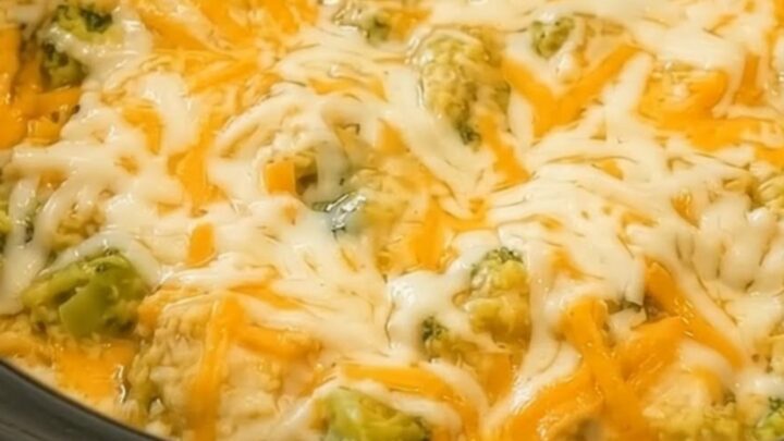 A black slow cooker filled with creamy chicken and rice, topped with melted yellow and white cheddar cheese and tender