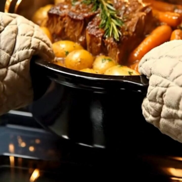 A steaming, tender chuck roast served with glazed baby potatoes and carrots on a white plate.