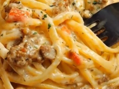 A close-up of creamy garlic butter beef linguine in a skillet with tomatoes and parsley.