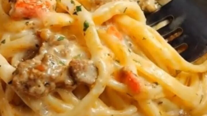 A close-up of creamy garlic butter beef linguine in a skillet with tomatoes and parsley.