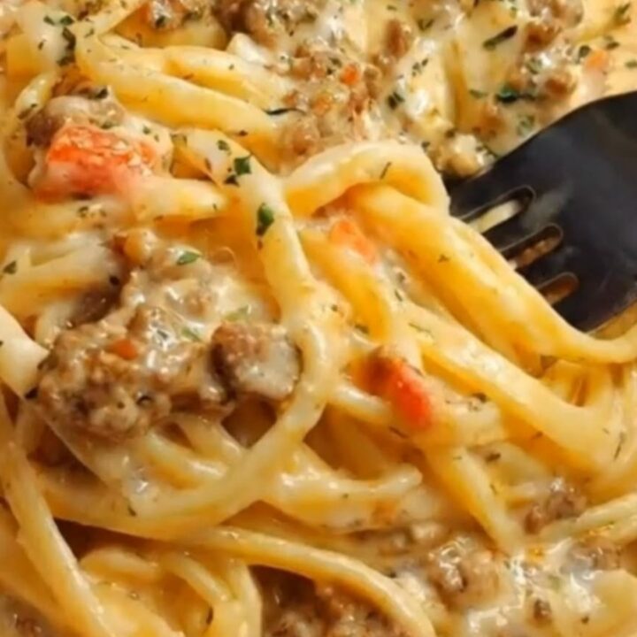 A close-up of creamy garlic butter beef linguine in a skillet with tomatoes and parsley.