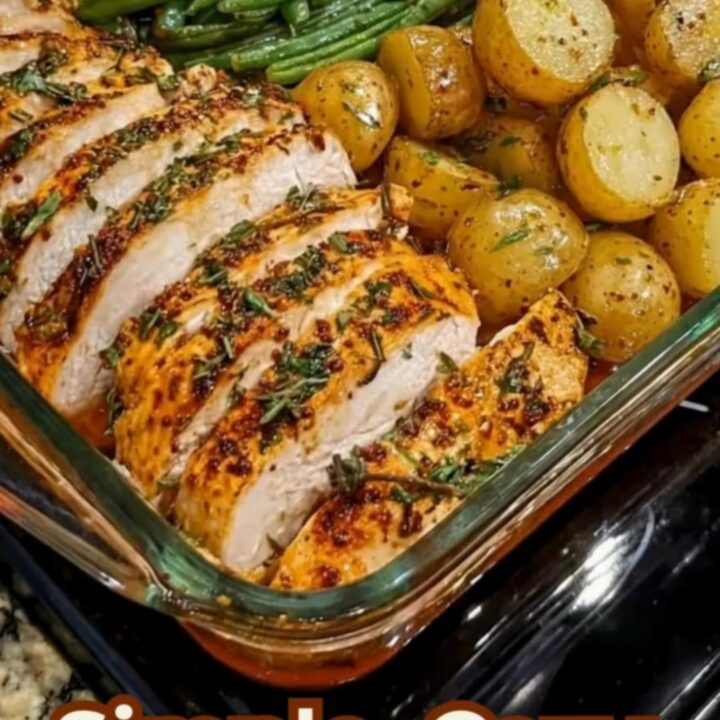 A rectangular glass baking dish filled with herb-crusted roasted chicken slices, golden baby potatoes