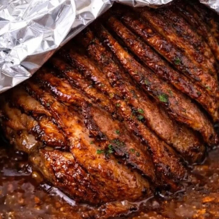 A close-up of a spiral-cut glazed ham with a shiny, dark brown sugar coating on a platter.
