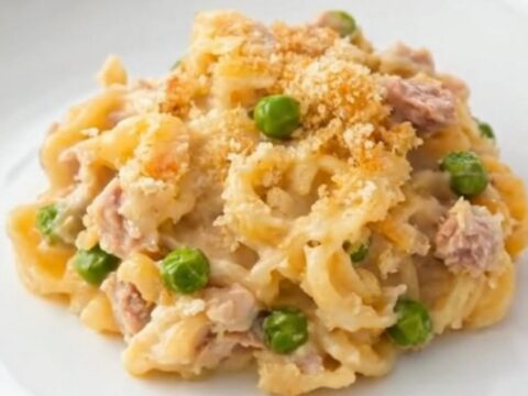 A creamy portion of tuna casserole with egg noodles, sweet peas, and a golden panko crust on a white plate